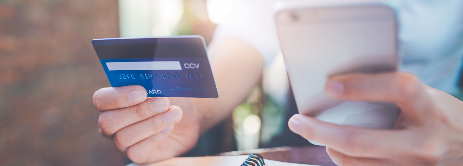 A person holding a credit card beside their cell phone